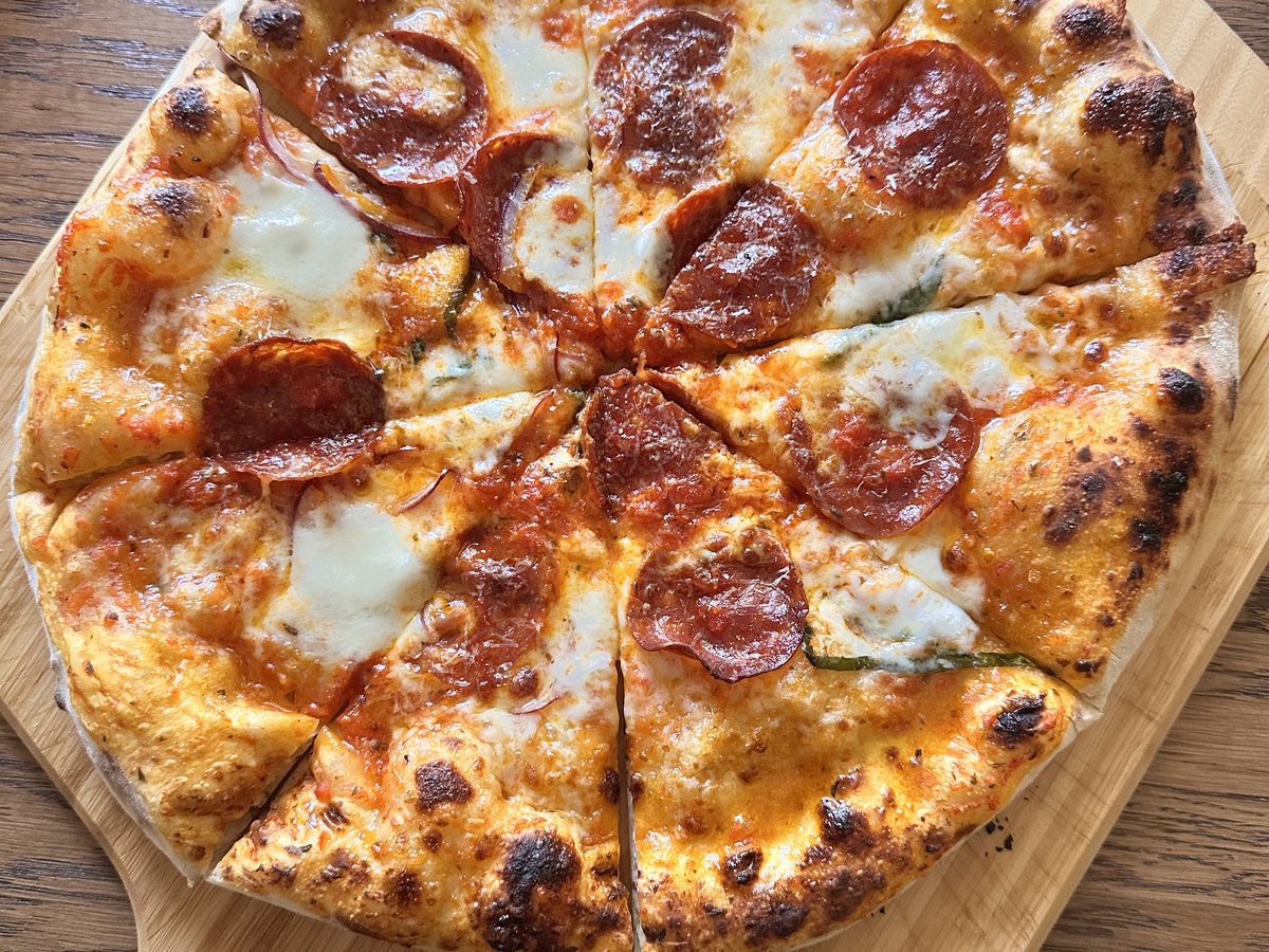New York style sourdough pizza sliced on a wooden board, showing a thin base and a bubbled, leopard-spotted rim